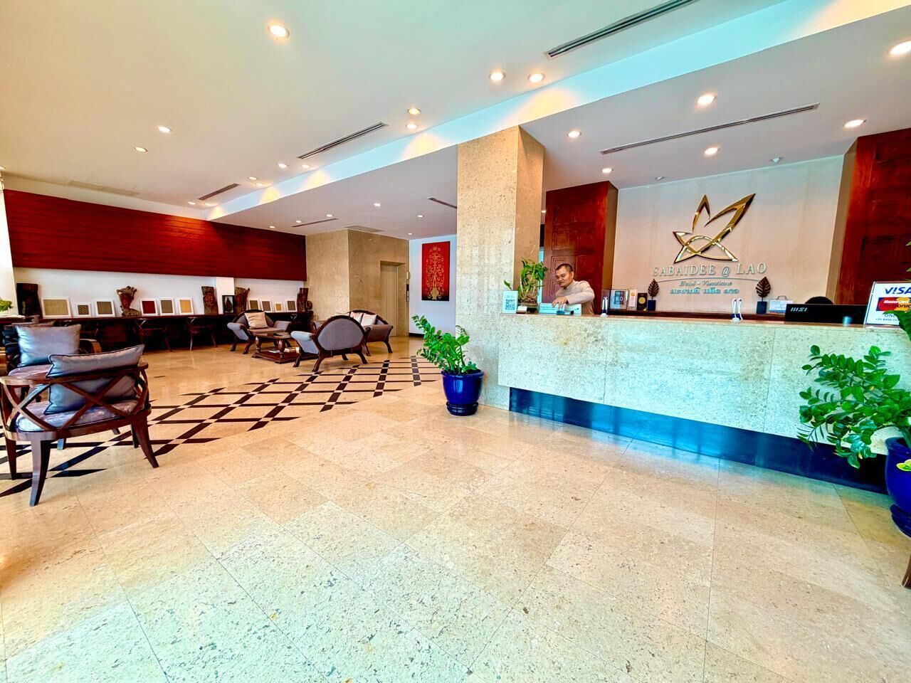 A hotel lobby with a reception desk, seating area, and potted plants.