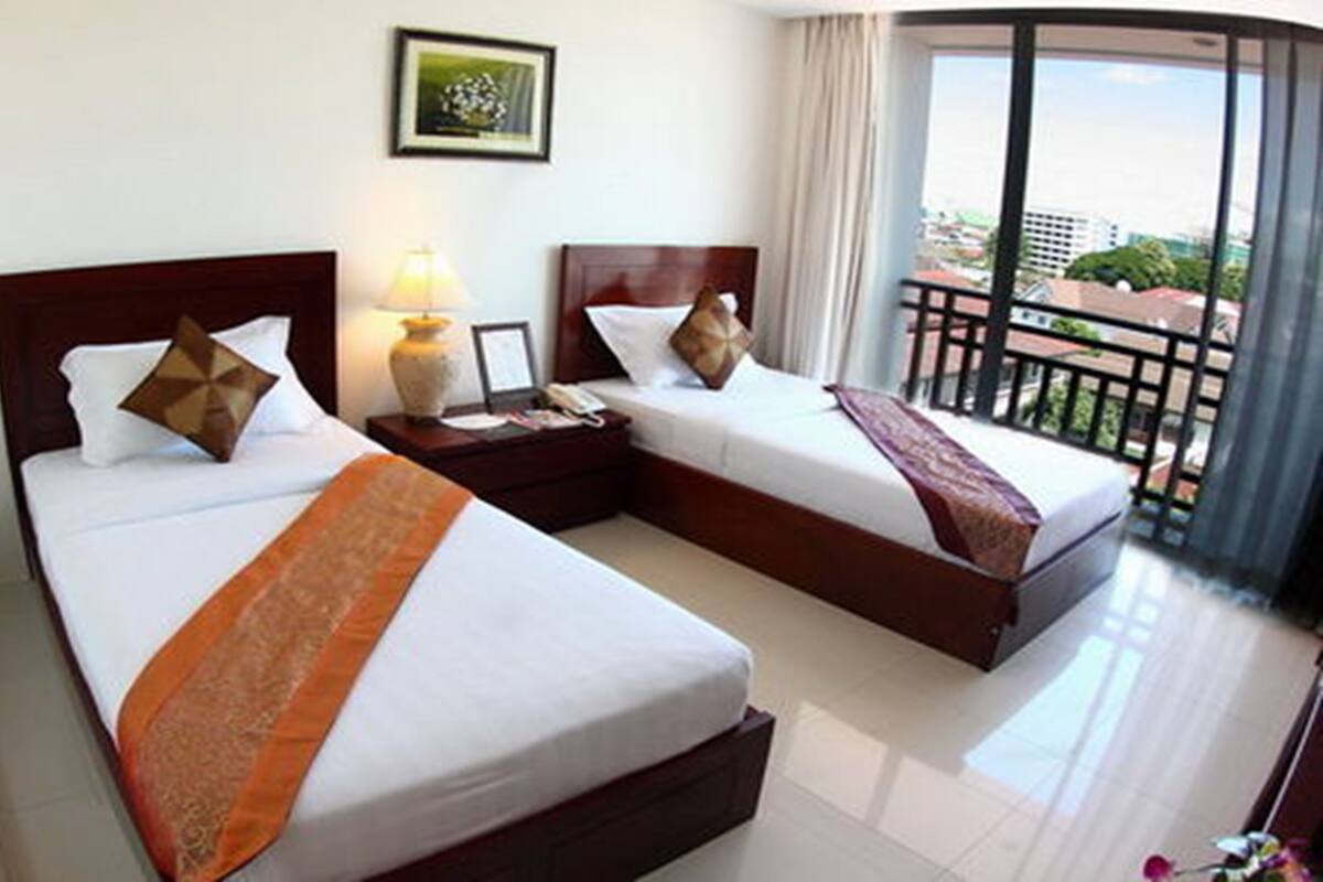 A hotel room with two beds, a nightstand, a lamp, and a view of the outside balcony.