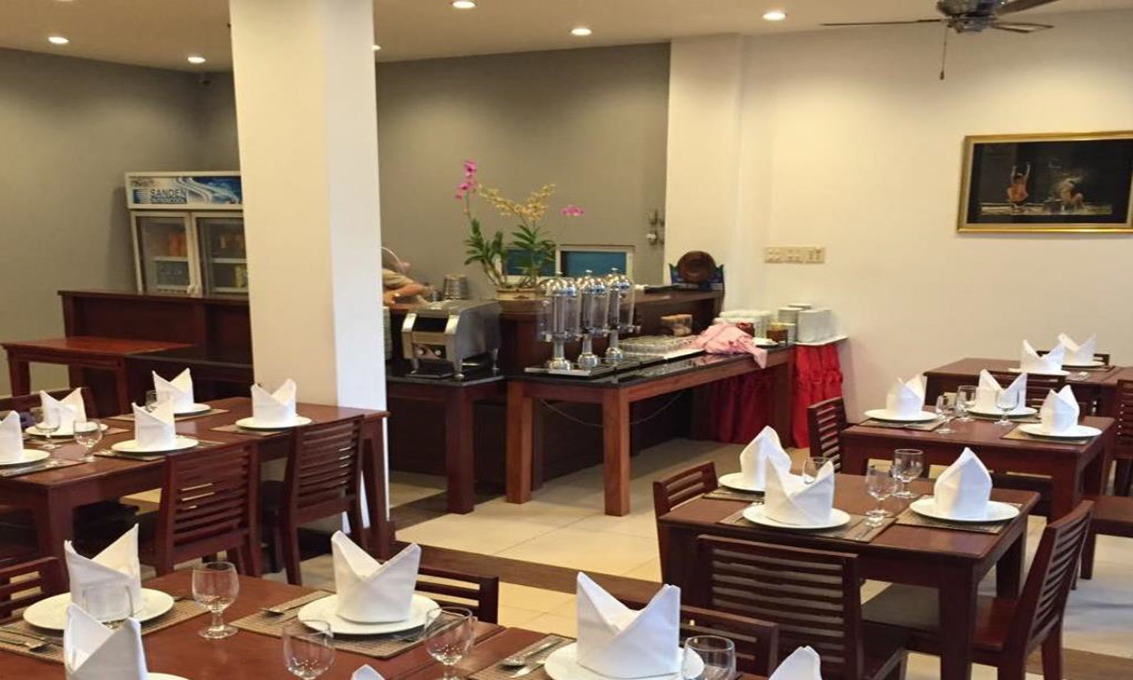Un espace repas avec des tables dressées pour le service, une machine à café et un arrangement floral.