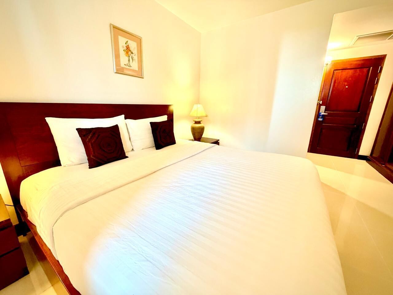 A large bed with white linens, a wooden headboard, a bedside lamp, and a framed picture on the wall.