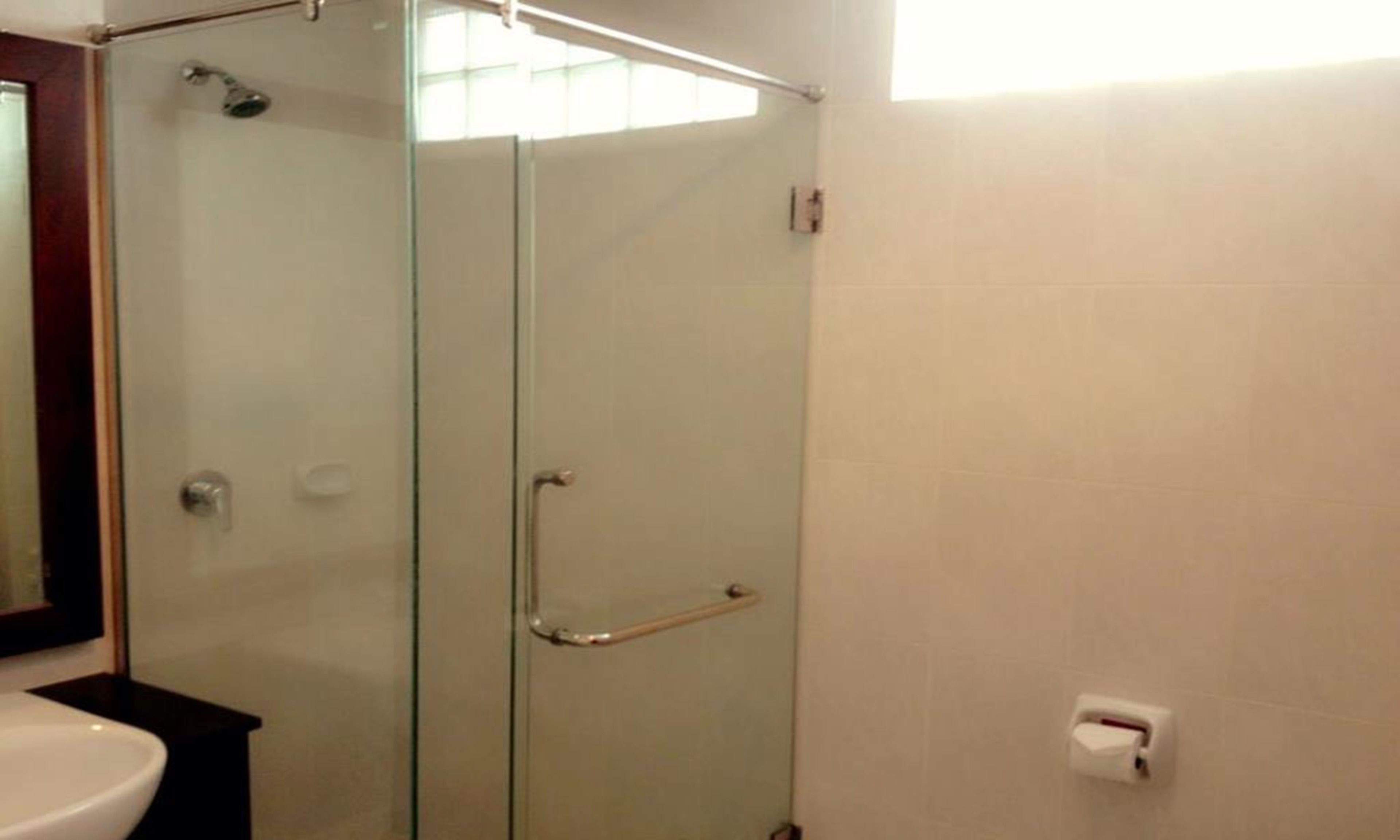 Cabina doccia con pareti in vetro, dotata di mancorrente, lavandino bianco e dispenser per asciugamani a parete.