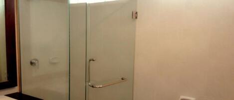 Cabina doccia con pareti in vetro, dotata di mancorrente, lavandino bianco e dispenser per asciugamani a parete.