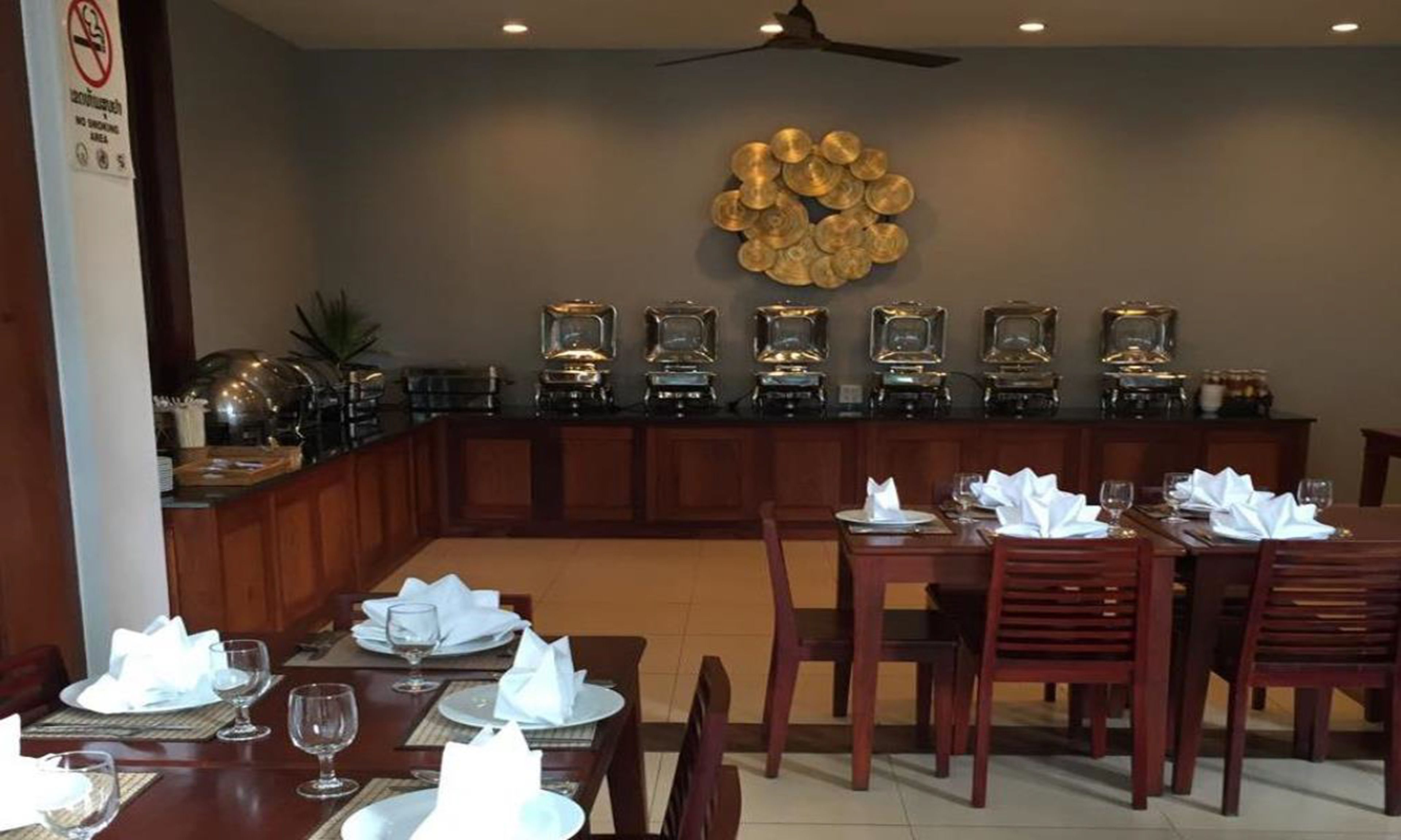A restaurant with a long counter, multiple tables set for dining, and a decorative wall with circular patterns.