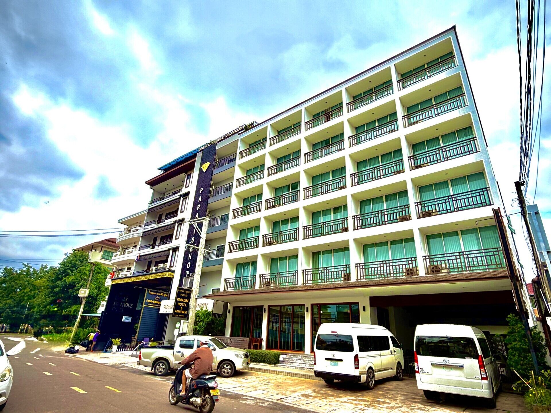 A multi-story hotel with balconies, a parking area, and a street view.