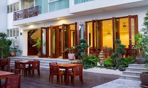 Un hotel con un área exterior cubierta que cuenta con mesas y sillas de madera, una escalera y plantas en macetas.
