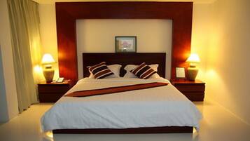 Quarto de hotel com uma cama grande, duas mesas de cabeceira com luminárias, um quadro na parede e uma cortina na janela.