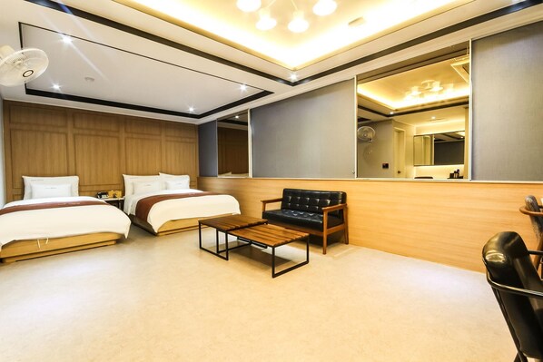 Una habitación de hotel moderna con dos camas, una mesa de centro de madera, un sillón de cuero negro y un espejo grande.