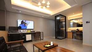 A modern hotel room with a living area featuring a sofa, a coffee table, and a TV. There is a kitchenette with a refrigerator, microwave, and a small dining table. - 500th Hotel (Mokpo)