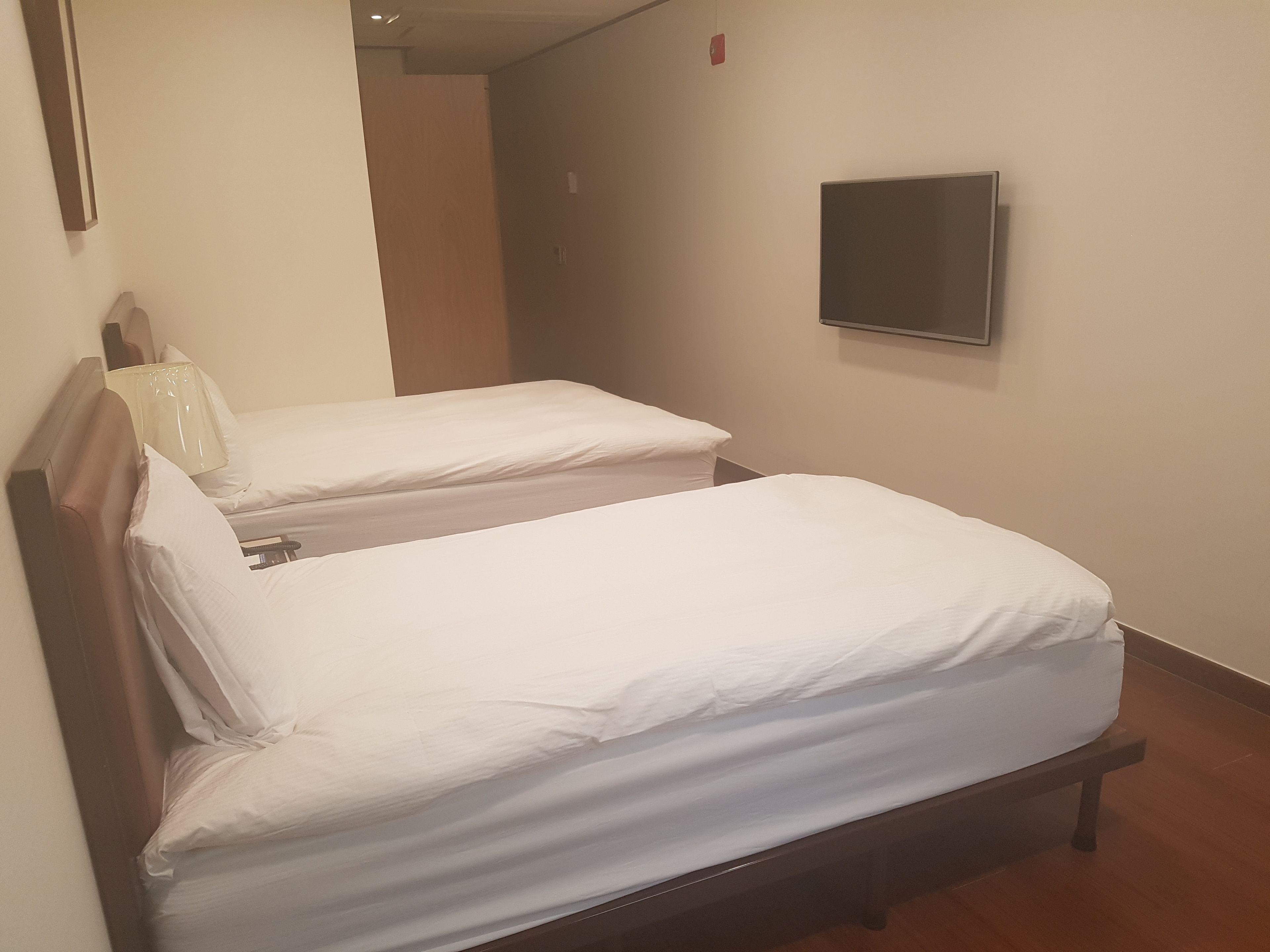 Dos camas individuales con cabeceros de madera y ropa de cama blanca en una habitación con un televisor de pantalla plana montado en la pared.