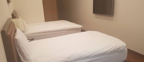Dos camas individuales con cabeceros de madera y ropa de cama blanca en una habitación con un televisor de pantalla plana montado en la pared.