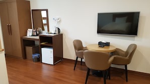 Une pièce compacte comprenant une armoire en bois, un petit coin cuisine, une table ronde avec deux chaises et un téléviseur à écran plat fixé au mur.