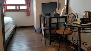 Une chambre d’hôtel compacte comprenant un lit simple, un bureau avec un ordinateur, une chaise et une petite table avec une machine à café.