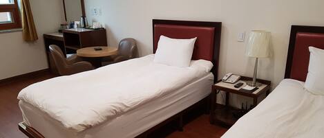 A hotel room with two single beds, a desk with a chair, a small table, a lamp, and a painting on the wall.