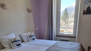 A hotel room with a bed, pillows, a window with a view, and a wall-mounted picture.