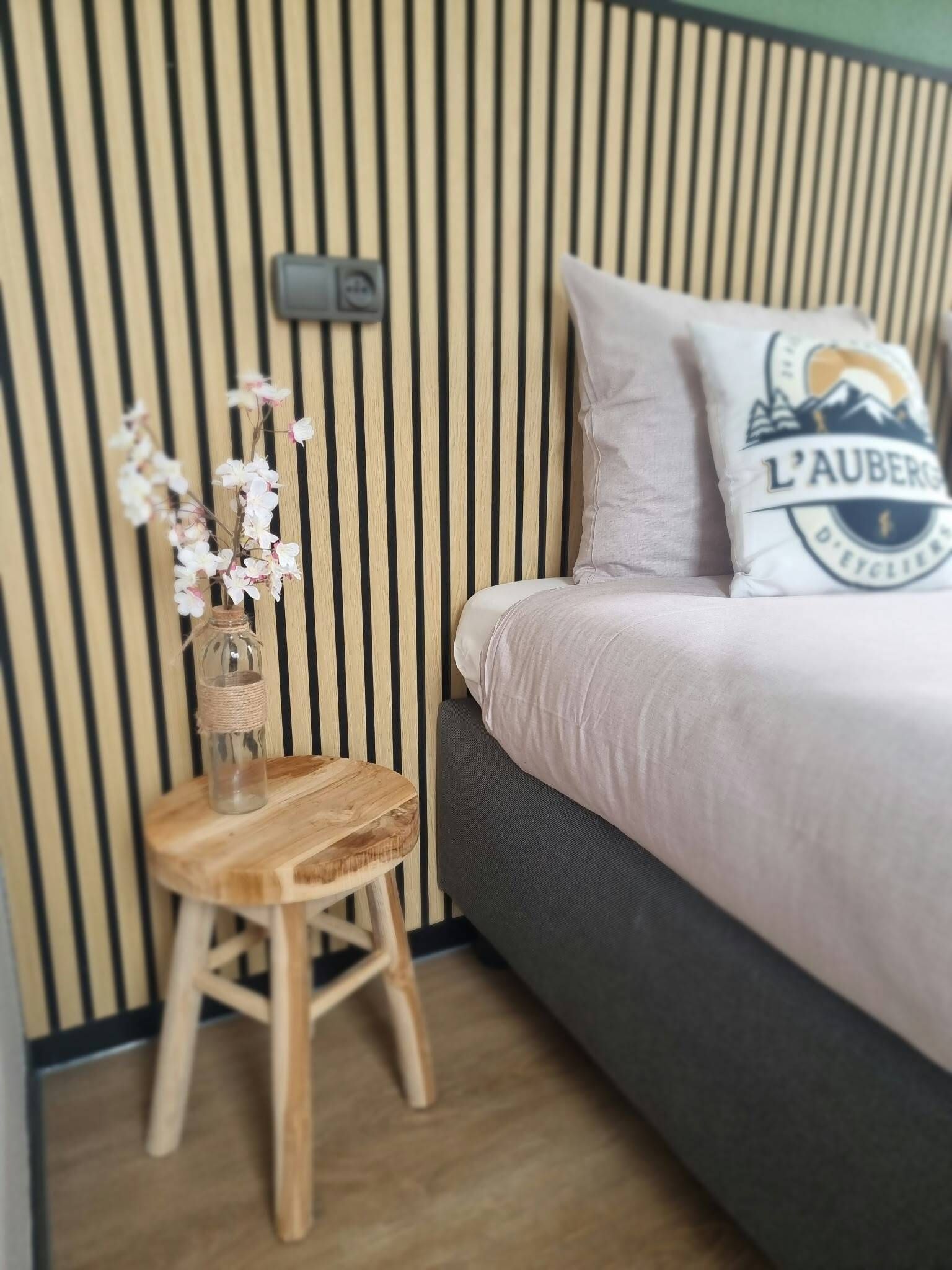 Une chambre à coucher avec un lit, un tabouret en bois et un interrupteur fixé au mur.