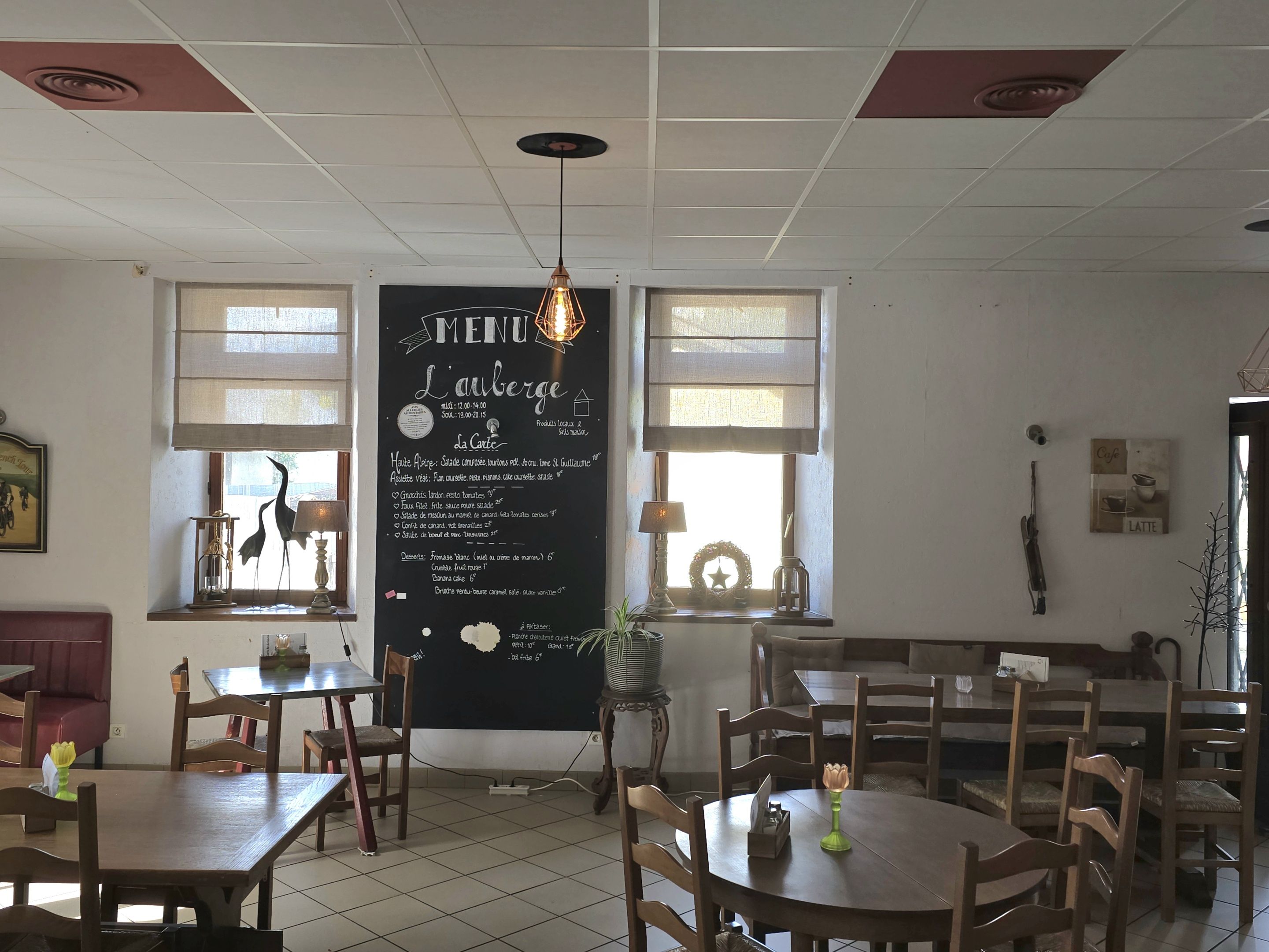 Interior de un restaurante con una pizarra de menú, mesas y sillas de madera, y un techo con iluminación empotrada.