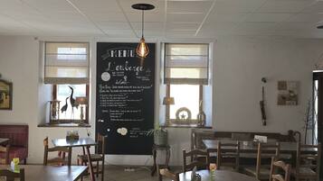 Interior de un restaurante con una pizarra de menú, mesas y sillas de madera, y un techo con iluminación empotrada.