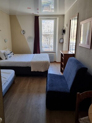 Una habitación con una cama, un sofá, una mesita y un ventanal con vista a árboles.