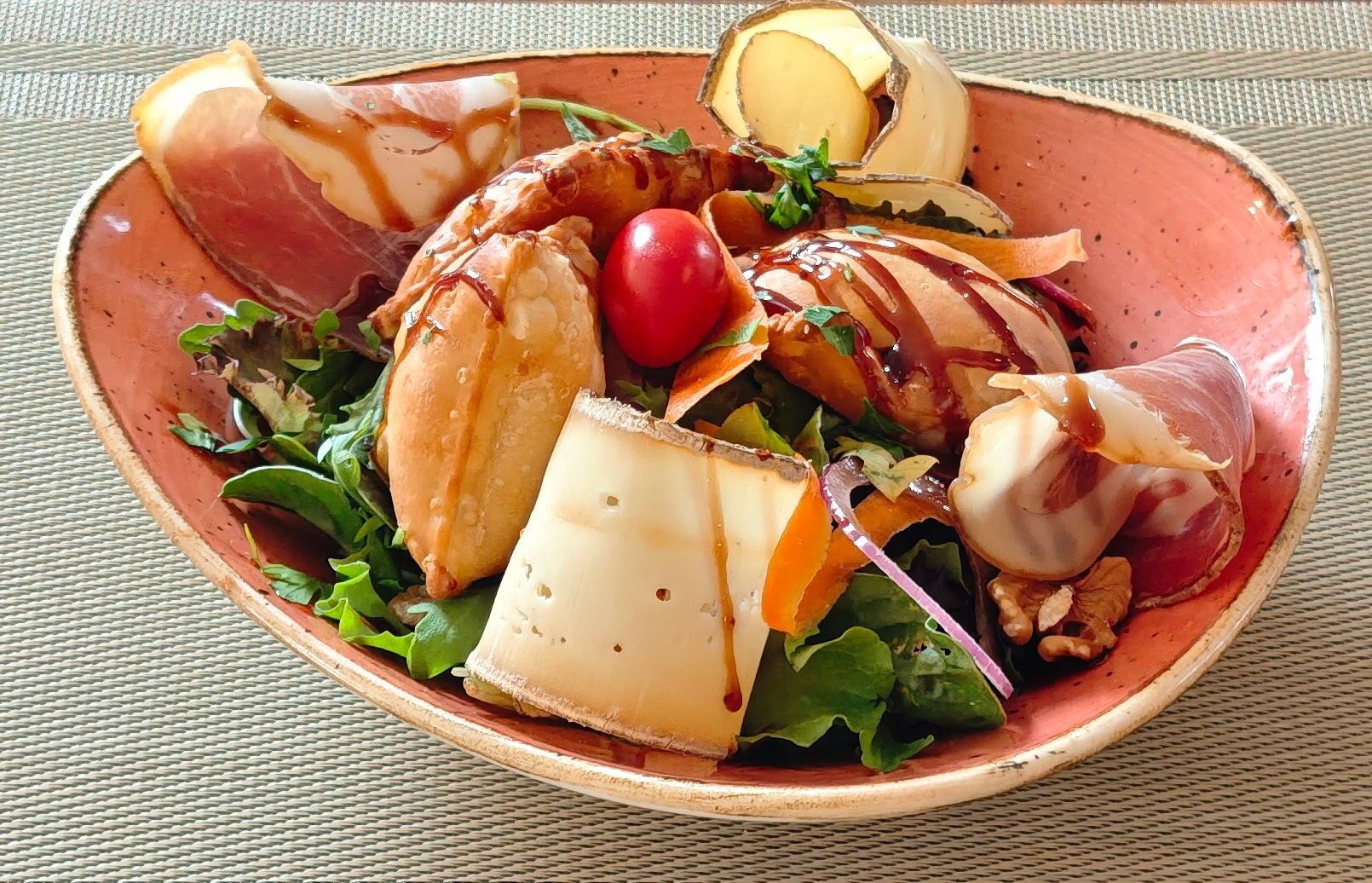 Un plato de comida con diferentes carnes, queso y un tomate cherry.