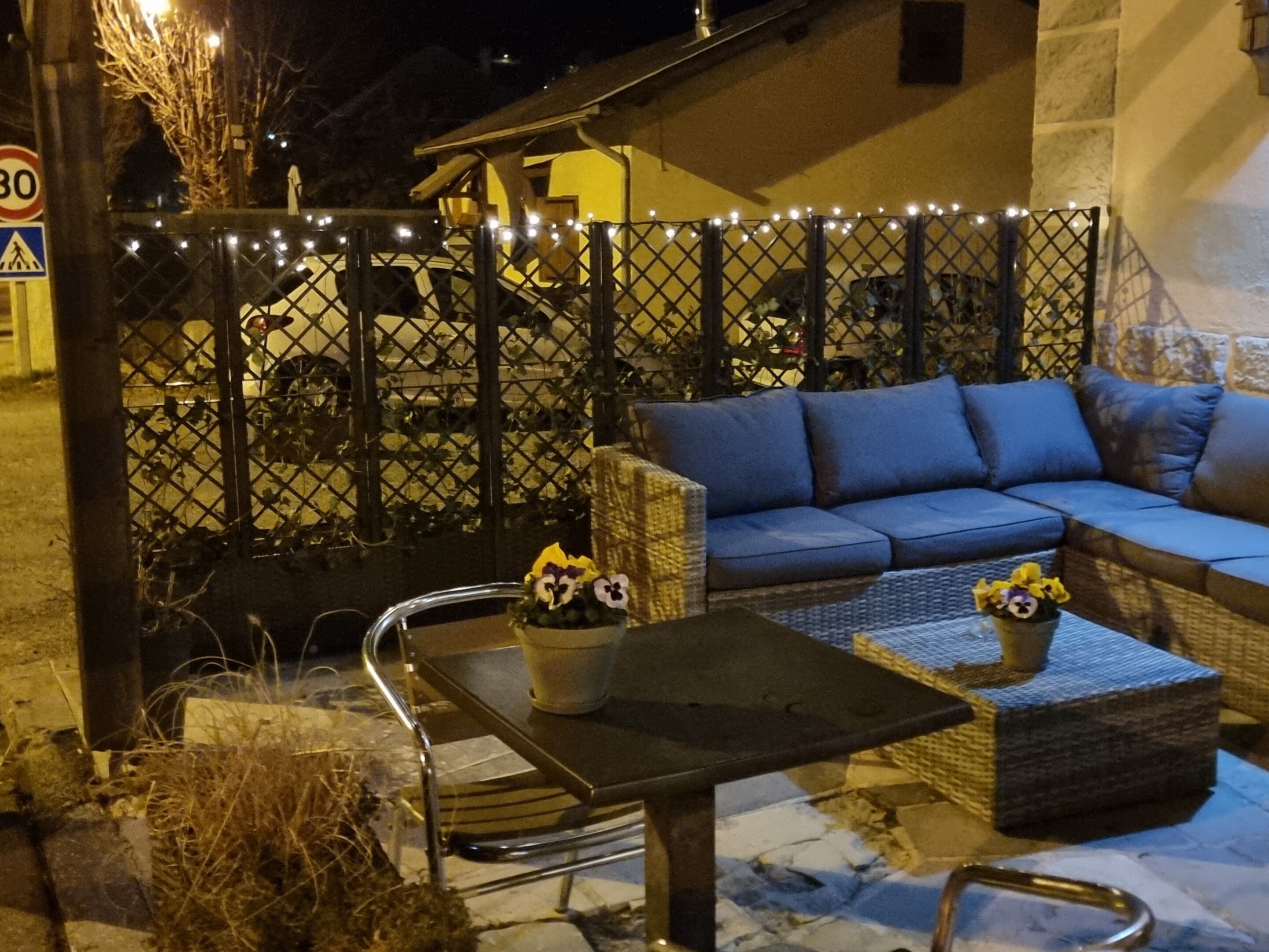 A cozy outdoor seating area with a sofa and a table, surrounded by a decorative fence with lights.
