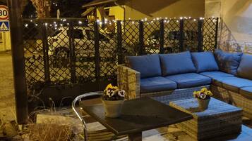 A cozy outdoor seating area with a sofa and a table, surrounded by a decorative fence with lights.