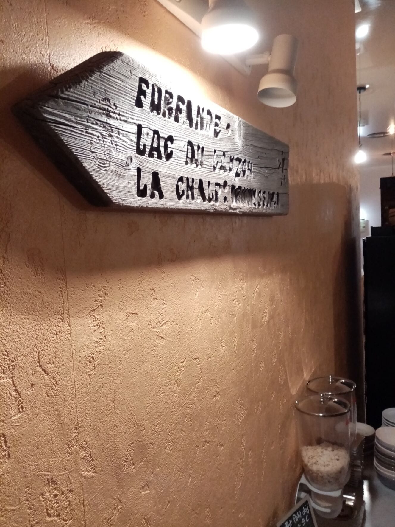 Uma placa de madeira com texto em idioma estrangeiro, uma parede texturizada e um recipiente de vidro com etiqueta.