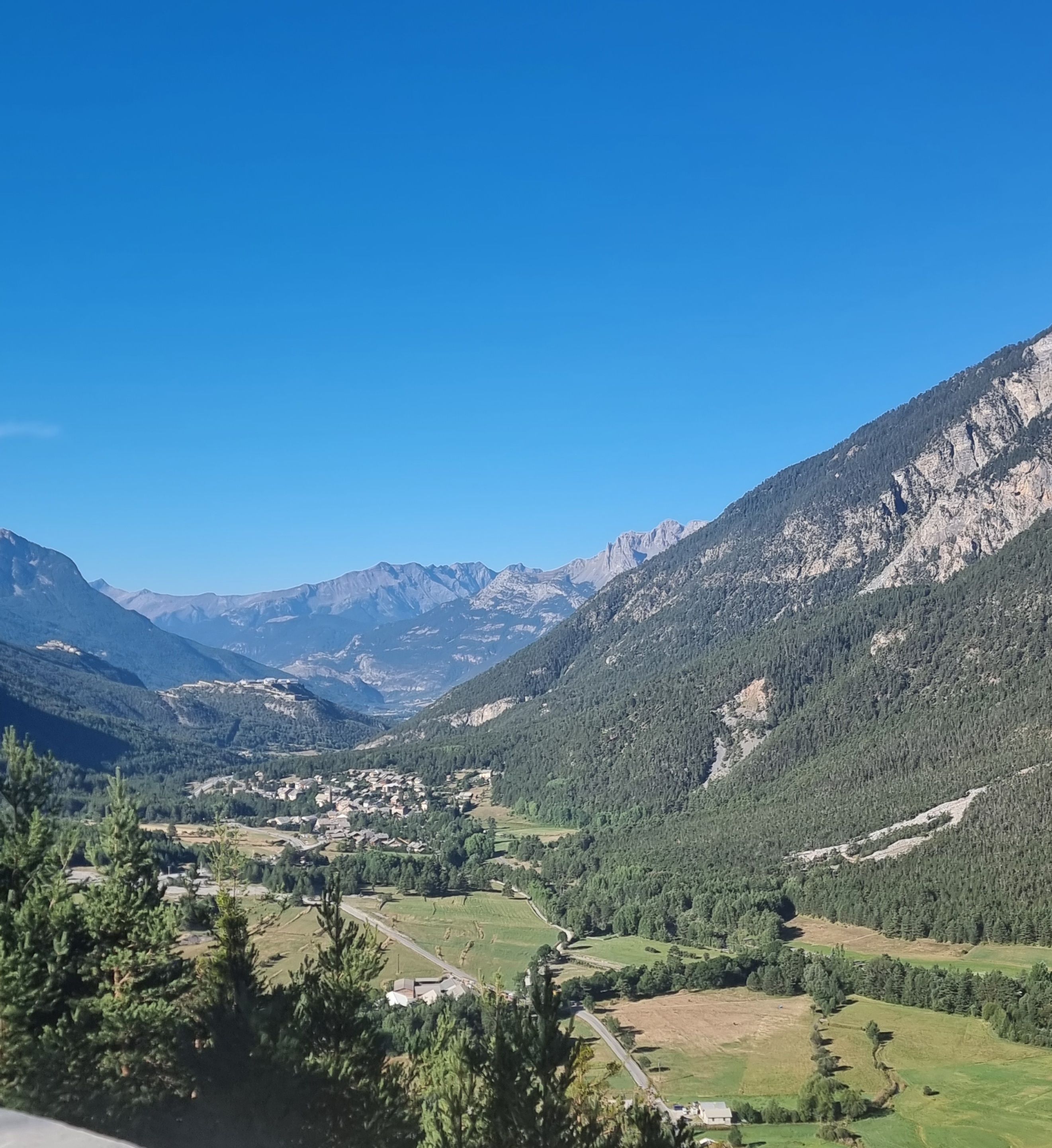 Un paisaje montañoso con un valle, un pequeño poblado y una carretera.