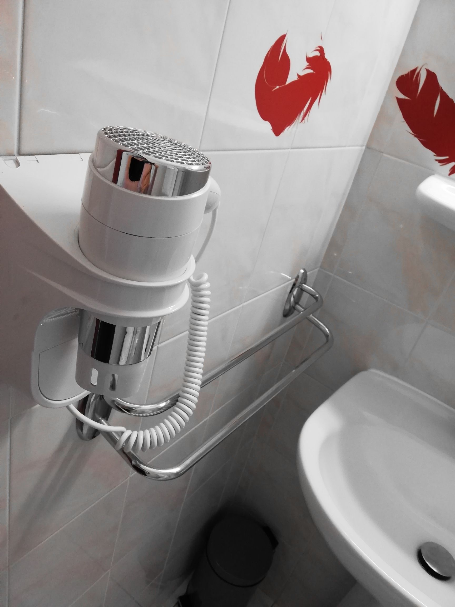 Un baño con lavamanos blanco, toallero y secador de pelo montado en la pared.