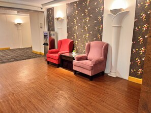 Una habitación con dos sillones, una mesita y una pared decorativa con motivos florales.