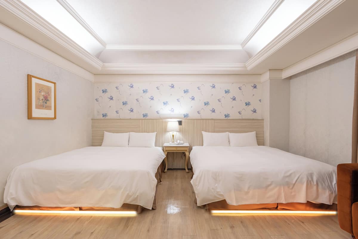 A hotel room with two beds, a nightstand, a lamp, and a framed picture on the wall.