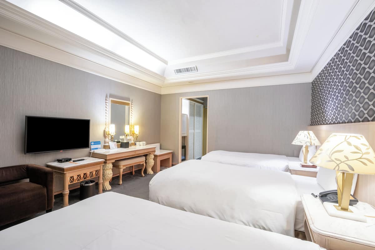 A hotel room with two beds, a TV, a desk with a lamp, and a mirror.