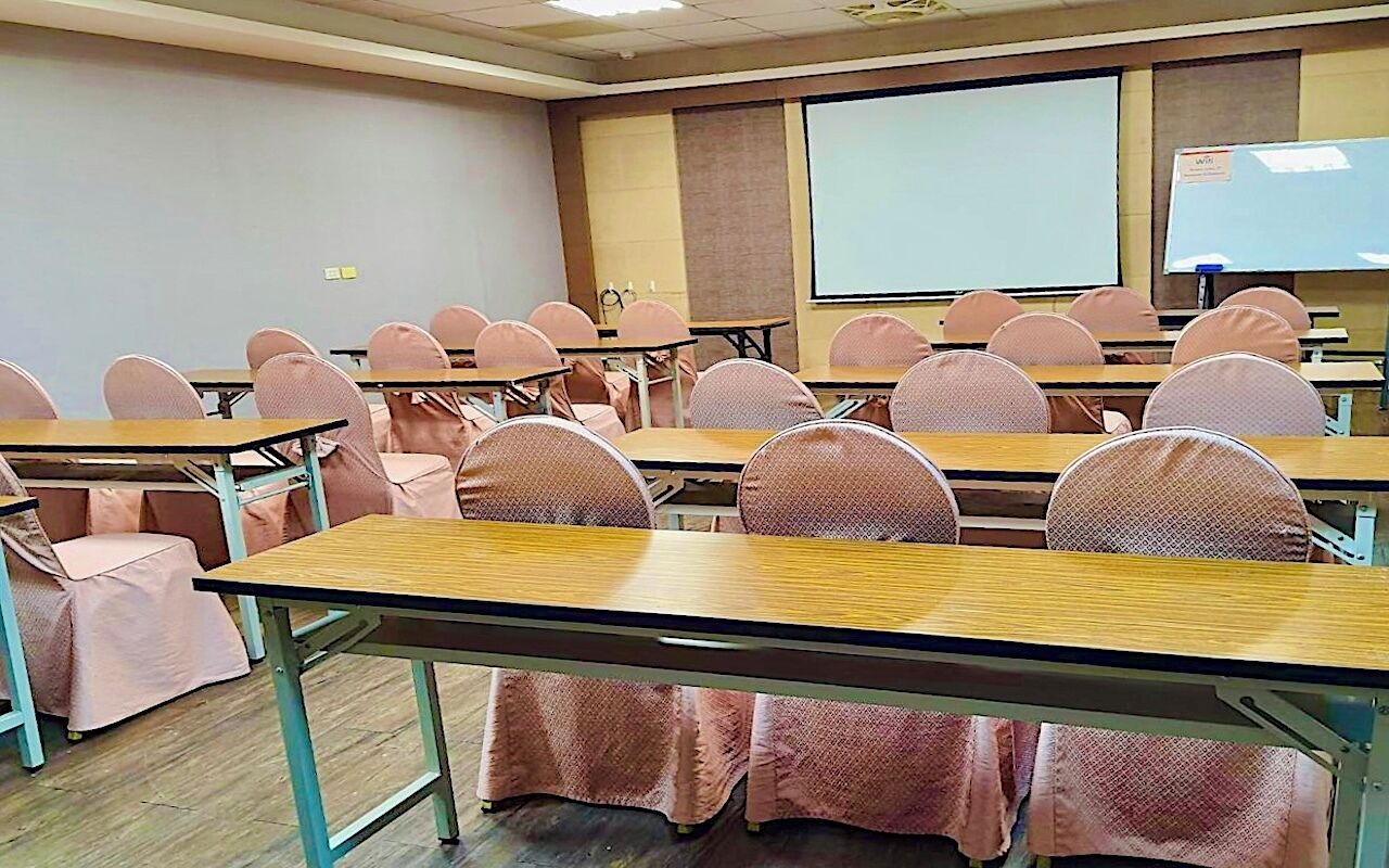 A classroom with rows of desks and chairs, a projector screen, and a whiteboard.