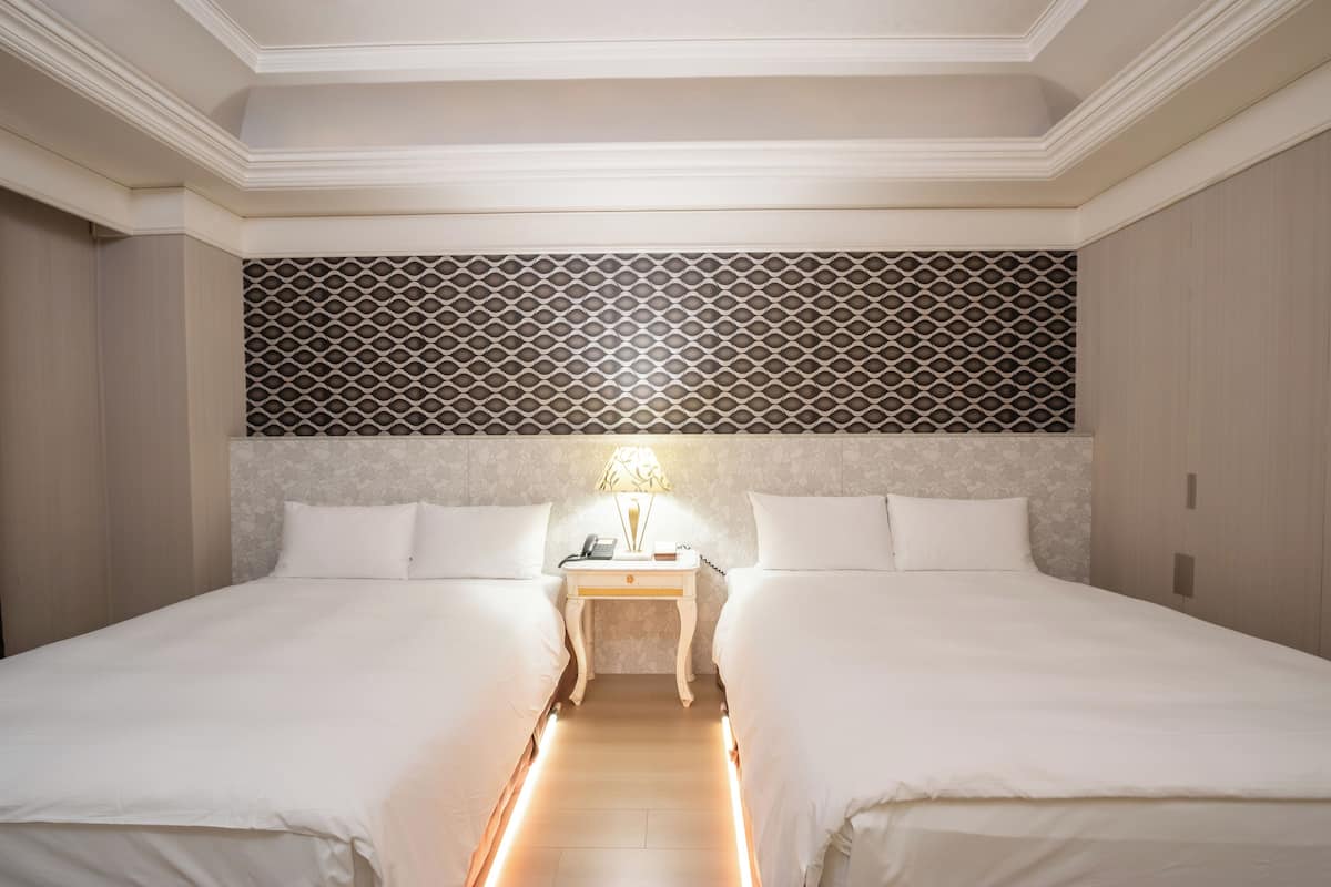 A hotel room with two beds, a nightstand with a lamp, and a patterned headboard.