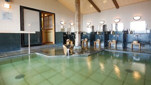 Un onsen japonés tradicional con varias zonas de baño, bancos de madera y un elemento central de agua.
