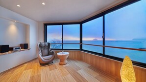 Una habitación moderna con un amplio ventanal, un sillón de masaje, una mesita redonda y un estante con altavoces.