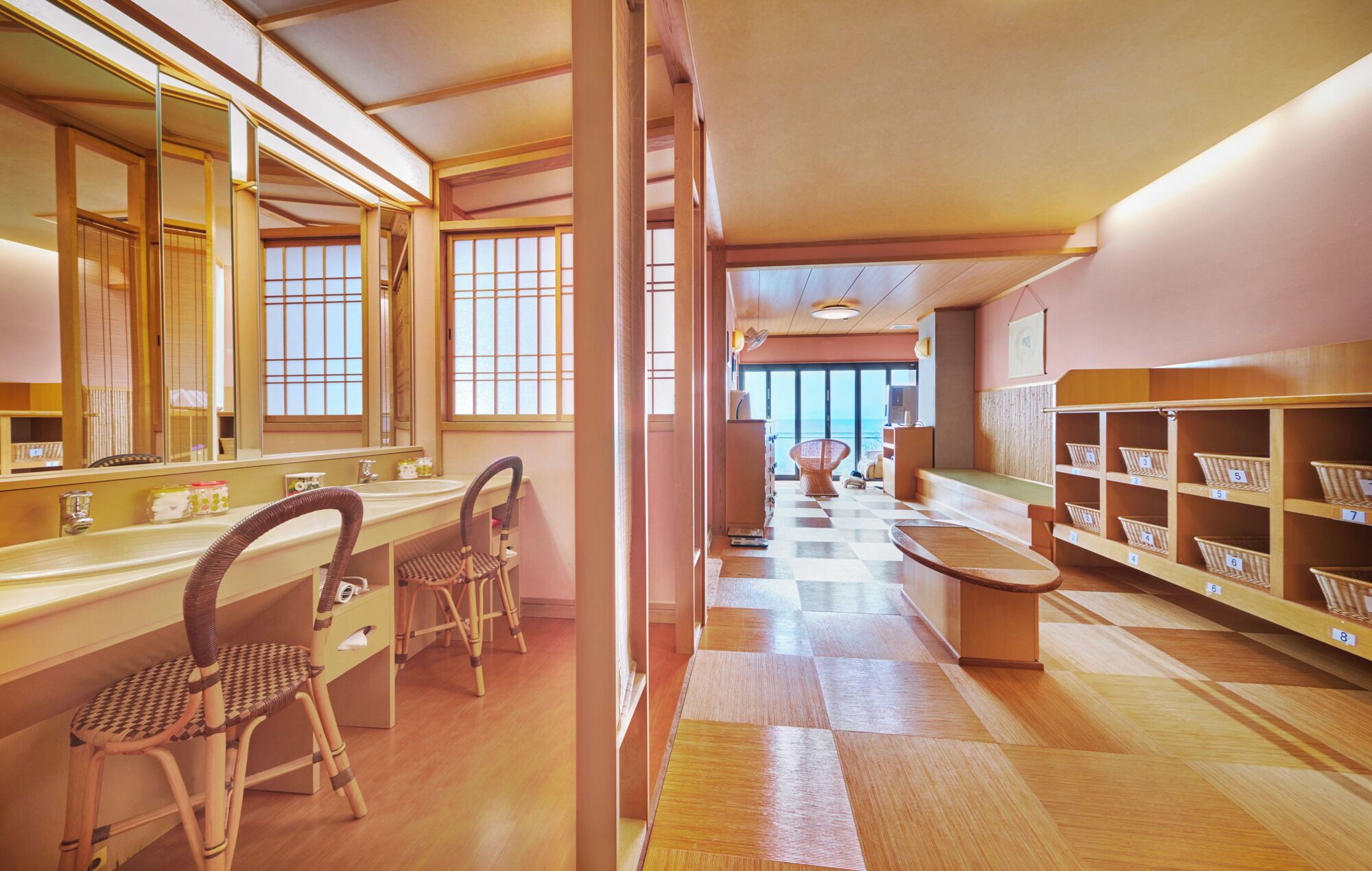 A hotel lobby with a checkered floor, a reception desk, wicker chairs, and a view of the sea through large windows.