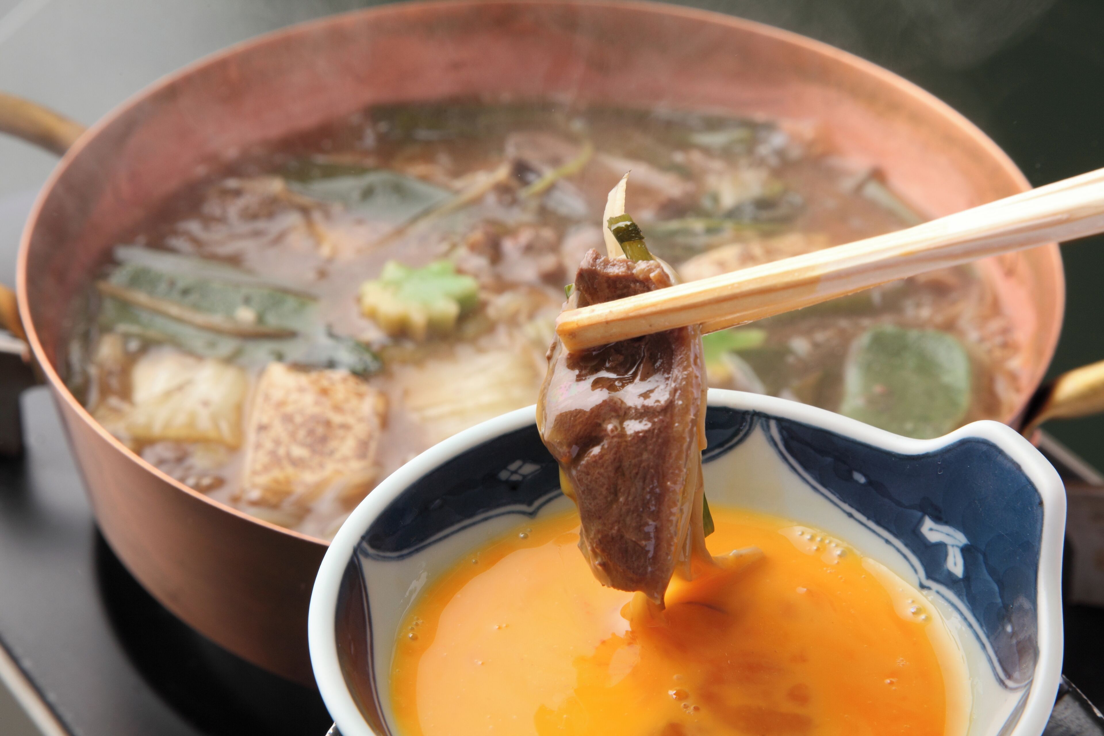 A bowl of soup with a piece of meat and chopsticks lifting it.