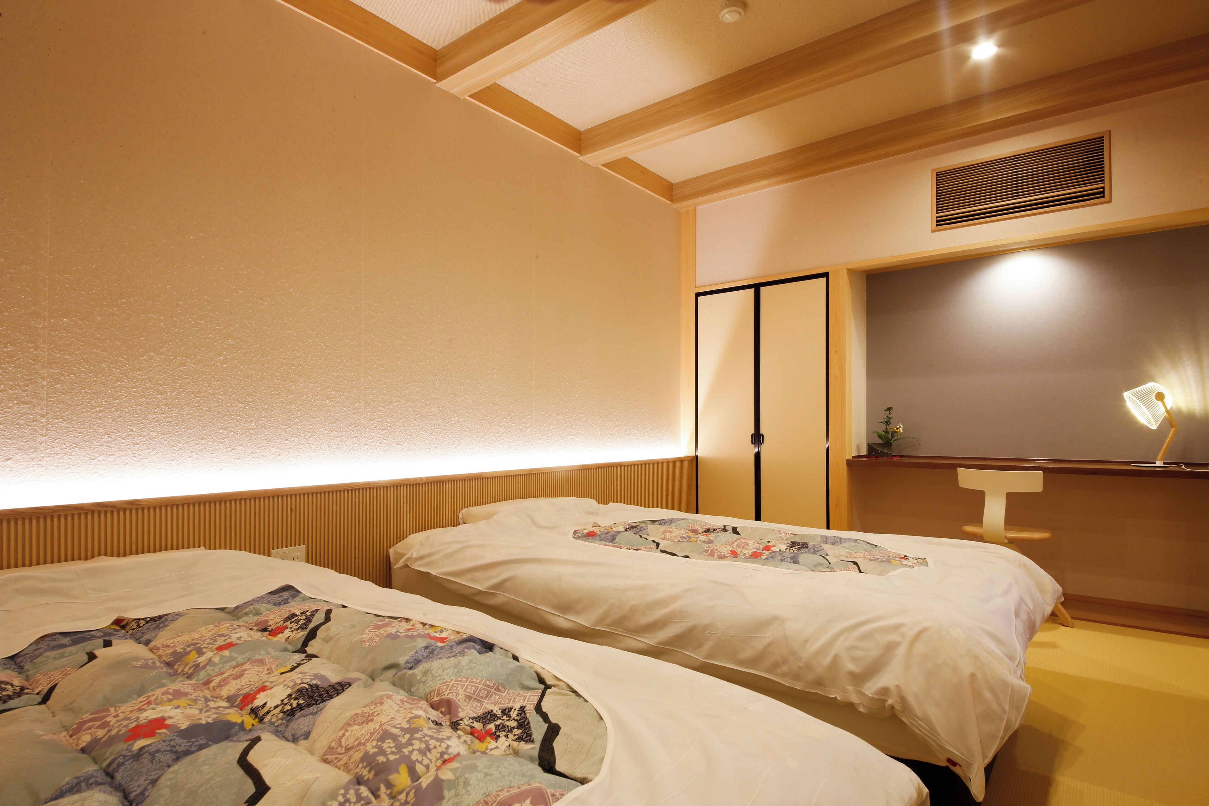 A hotel room with two beds, a bedside table, a lamp, and a wall-mounted shelf.