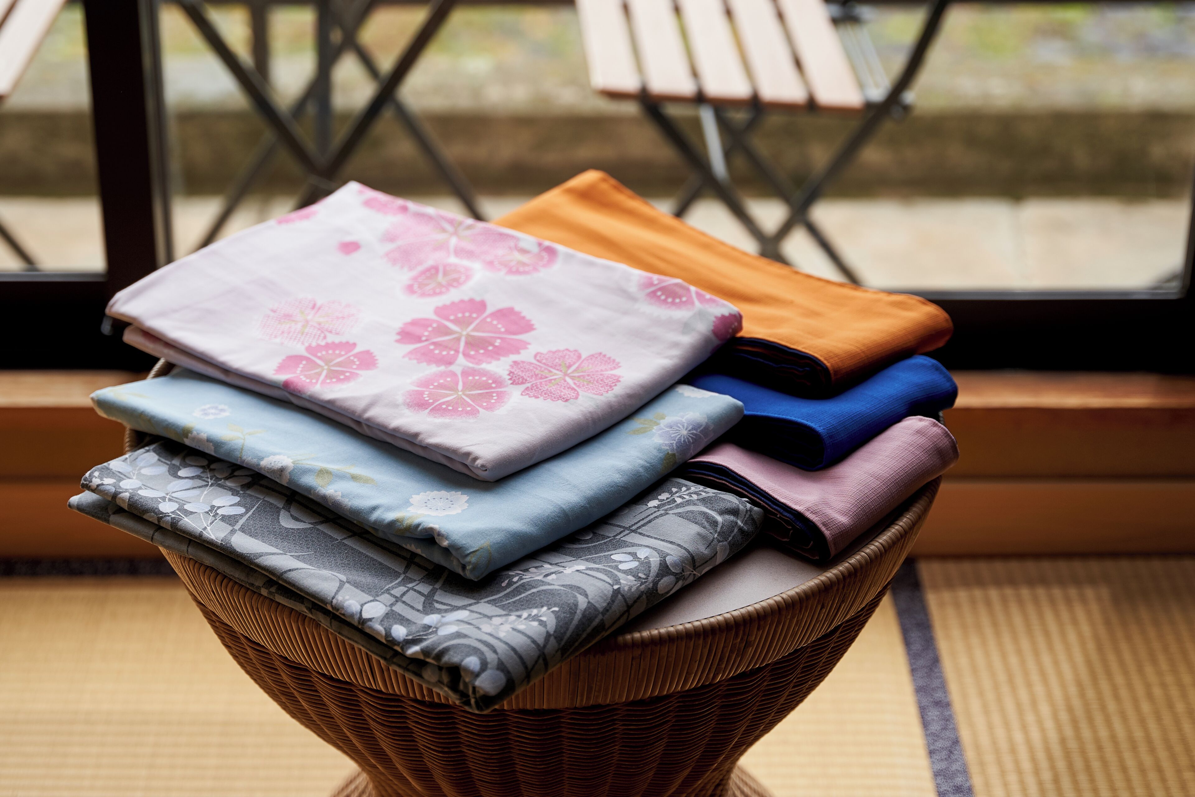 Una pila de textiles doblados en una cesta de mimbre sobre un estera de tatami.