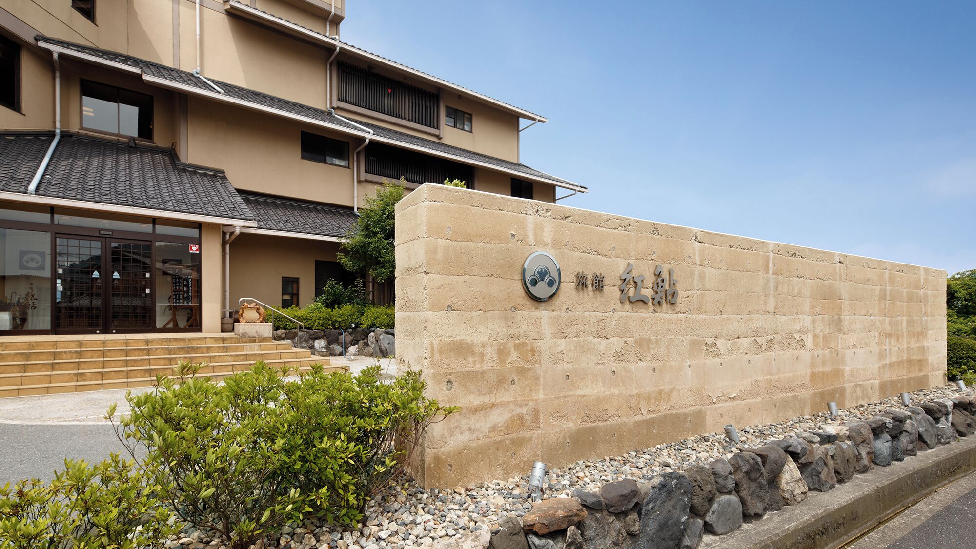 A building with a stone wall entrance, steps leading up to a door, and a clear sky.