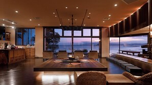 Un comedor espacioso con una gran mesa de madera, sillas de mimbre y vistas al mar a través de amplios ventanales.