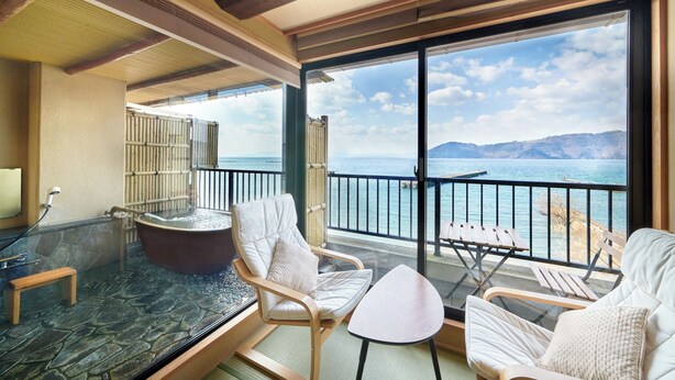 Un balcón con cerramiento de vidrio, jacuzzi y zona de estar con vista al mar.