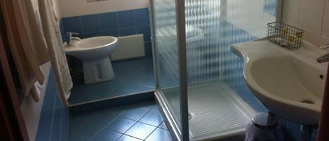 Baño con cabina de ducha de vidrio, inodoro y lavamanos.