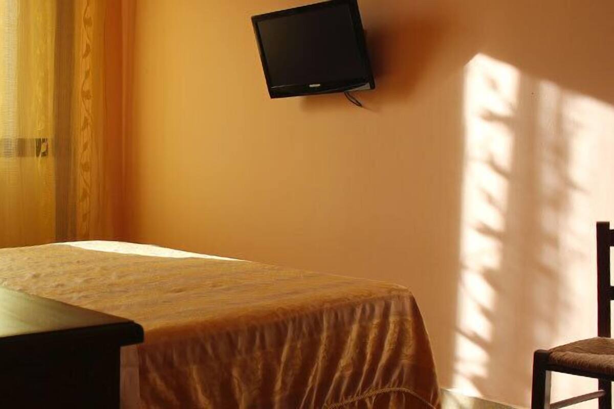 A hotel room with a bed, a bedside table with a lamp, a TV mounted on the wall, and a chair.