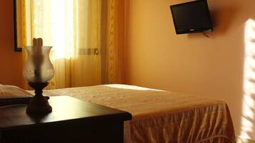 Una habitación de hotel con cama, una mesita de noche con lámpara, un televisor en la pared y una silla.