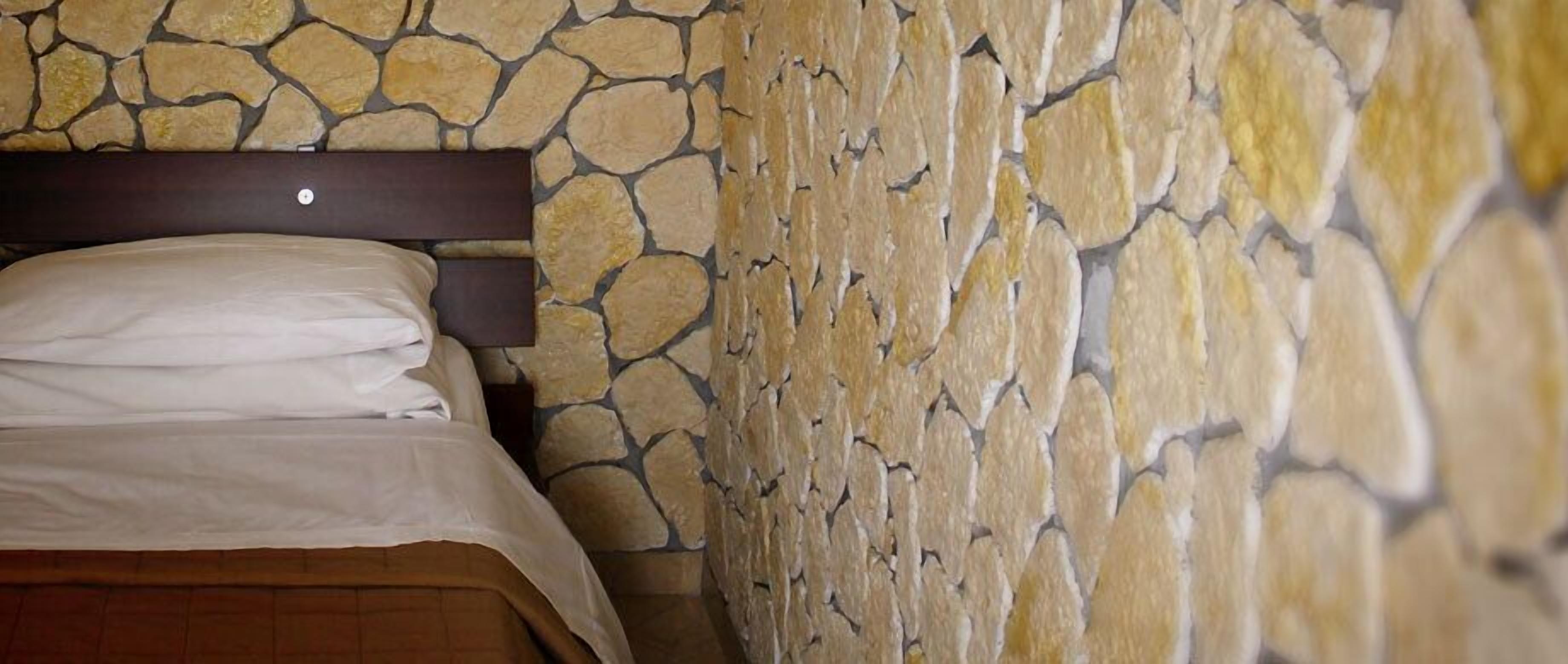 Cama com lençóis brancos em frente a uma parede de pedra.