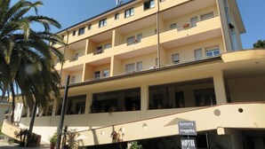 A multi-story hotel with balconies, a sign indicating it offers a bar and restaurant, and a sign for a trattoria and fruttu shop.