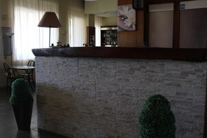 Zona de recepción con pared de piedra, mostrador, lámpara, silla y planta en maceta.