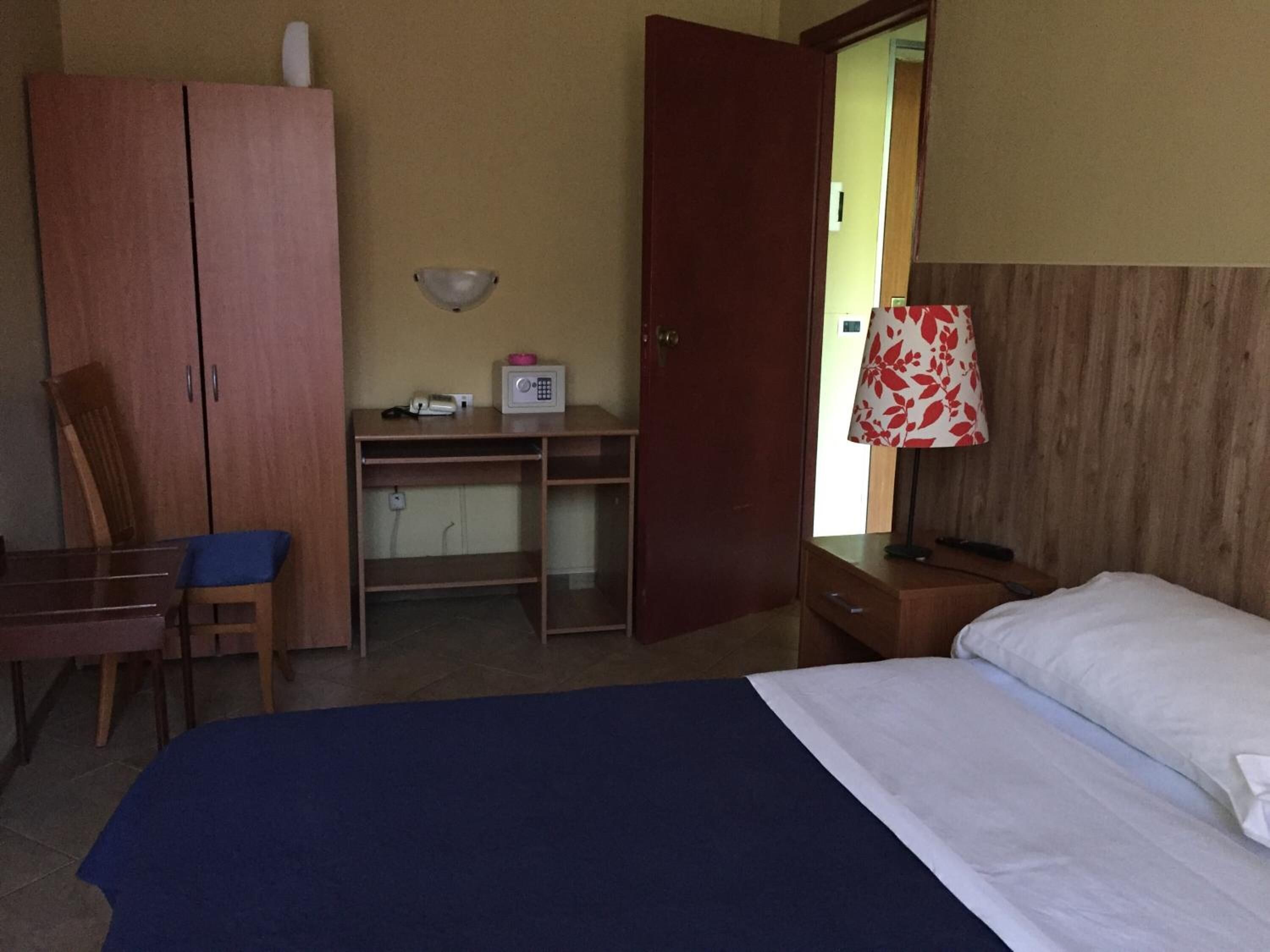 Une chambre d’hôtel comprenant un lit, un bureau avec une chaise, une armoire et une lampe.