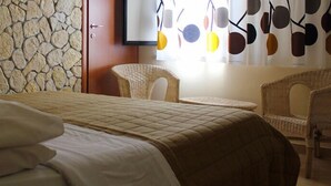 A bedroom with a stone wall, a bed with a quilted cover, two wicker chairs, and a window with a curtain featuring circular patterns.